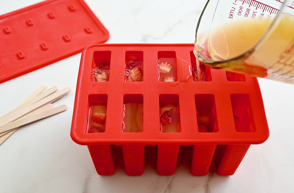 Boozy mix being poured from a liquid measuring cup into silicone molds