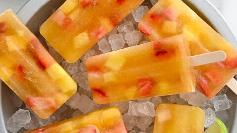 A top-down view of Peach Sangria Popsicles over ice in a pie plate next to fresh strawberries and a lime cut open in half