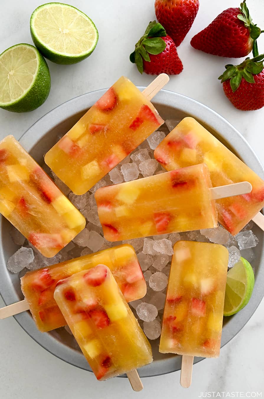 A top-down view of Peach Sangria Popsicles over ice in a pie plate next to fresh strawberries and a lime cut open in half