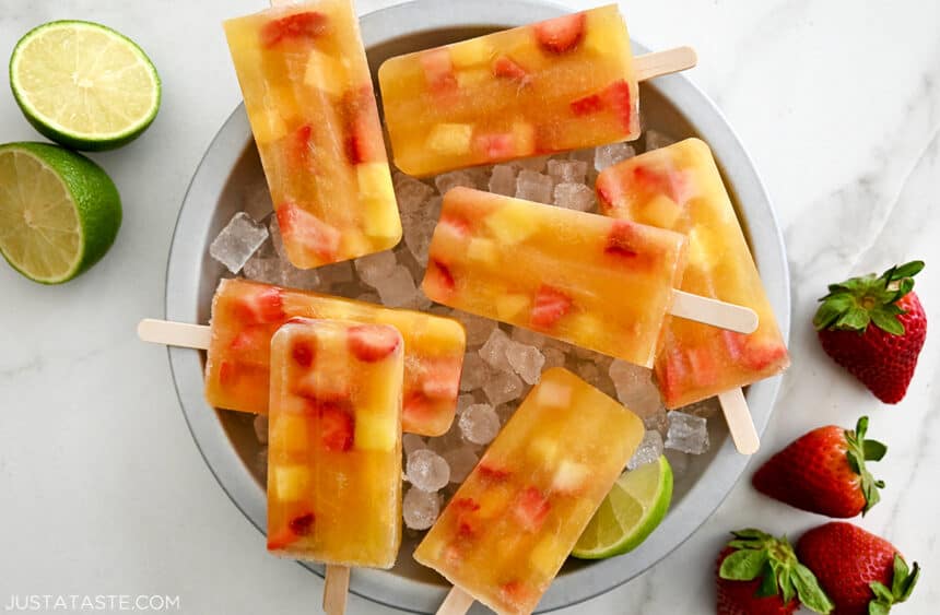 Easy Peach Sangria Popsicles with visible chunks of fresh fruit over ice in a pie plate that's next to fresh strawberries and a lime cut in half