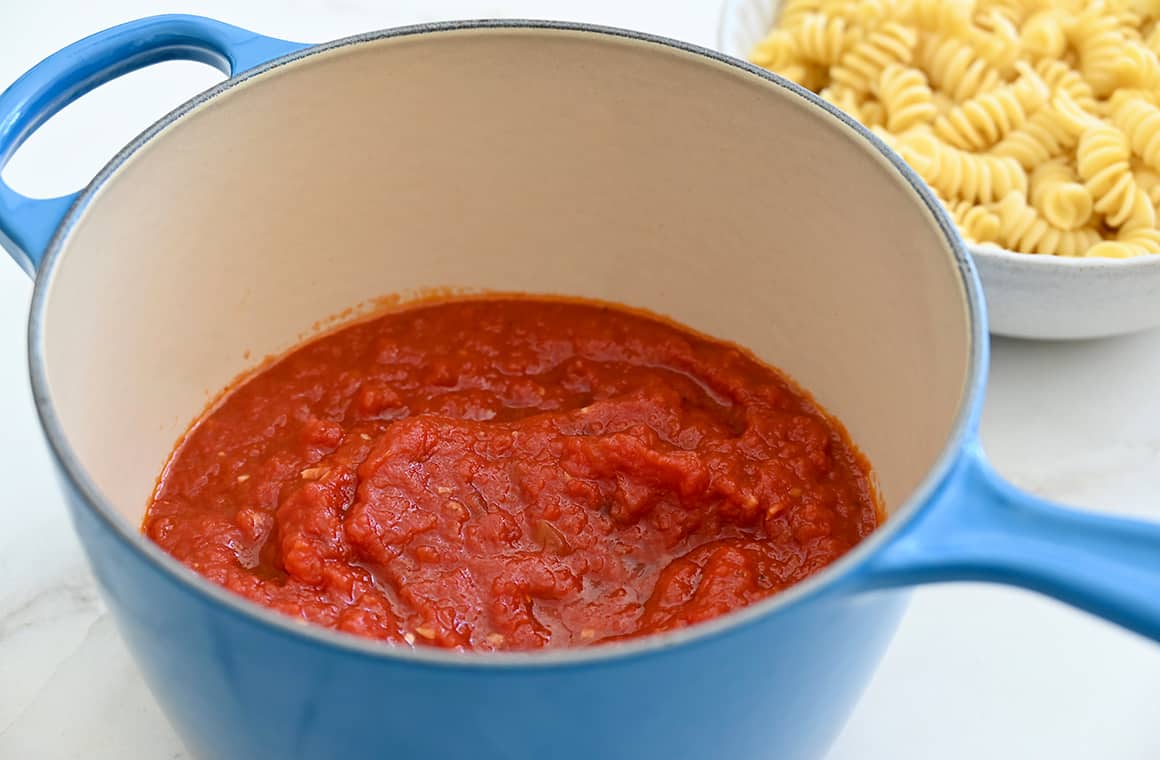 Quick homemade pasta sauce in a light blue stockpot next to a bowl with rotini noodles