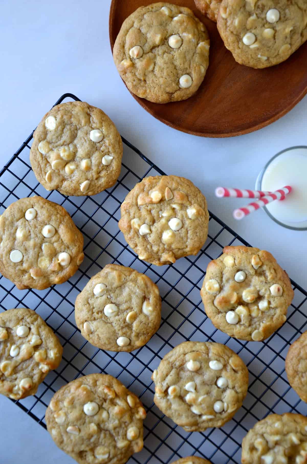 Cheesecake cookies with white chocolate chips cooling on a wire rack next to a glass of milk.