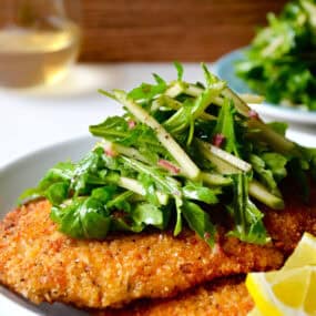 Chicken Milanese (crispy, breaded chicken cutlets) on a plate topped with an apple and arugula salad.