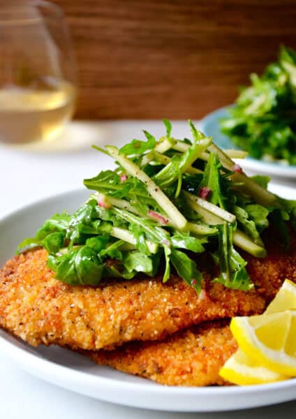 Chicken Milanese (crispy, breaded chicken cutlets) on a plate topped with an apple and arugula salad.