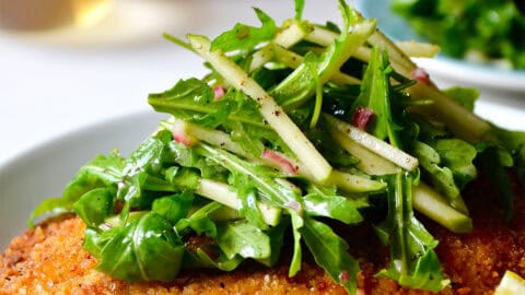 Chicken Milanese (crispy, breaded chicken cutlets) on a plate topped with an apple and arugula salad.