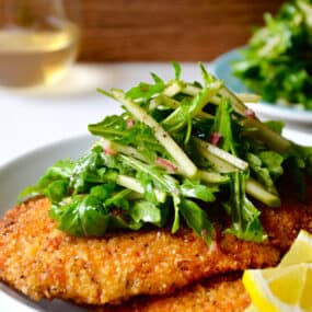 Chicken Milanese with Green Apple Salad on a white dinner plate with lemon wedges