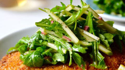 Chicken Milanese with Green Apple Salad on a white dinner plate with lemon wedges