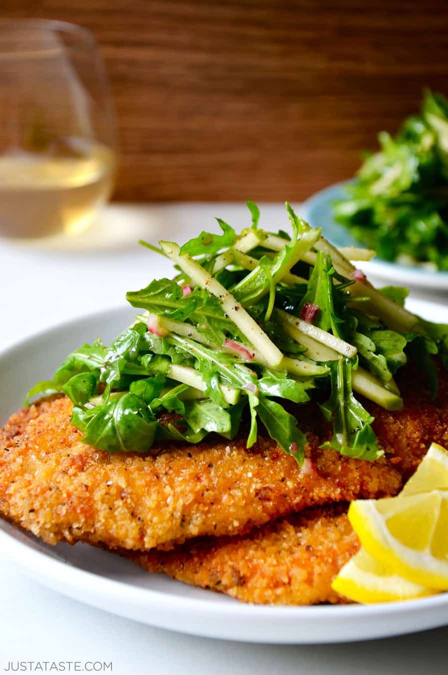 Chicken Milanese with Green Apple Salad on a white dinner plate with lemon wedges