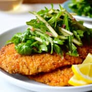 Chicken Milanese (breaded chicken cutlets) on a white plate topped with green apple and arugula salad.