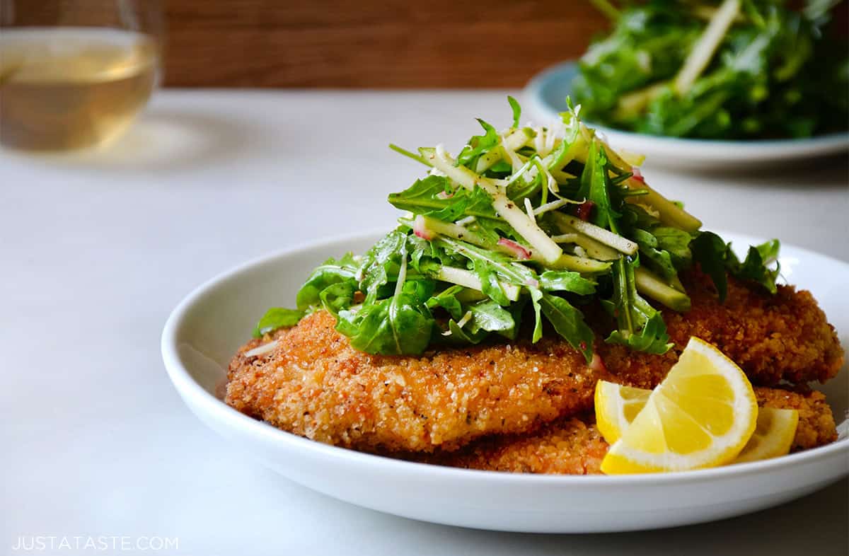 Chicken Milanese with arugula salad and lemon wedges on a dinner plate.