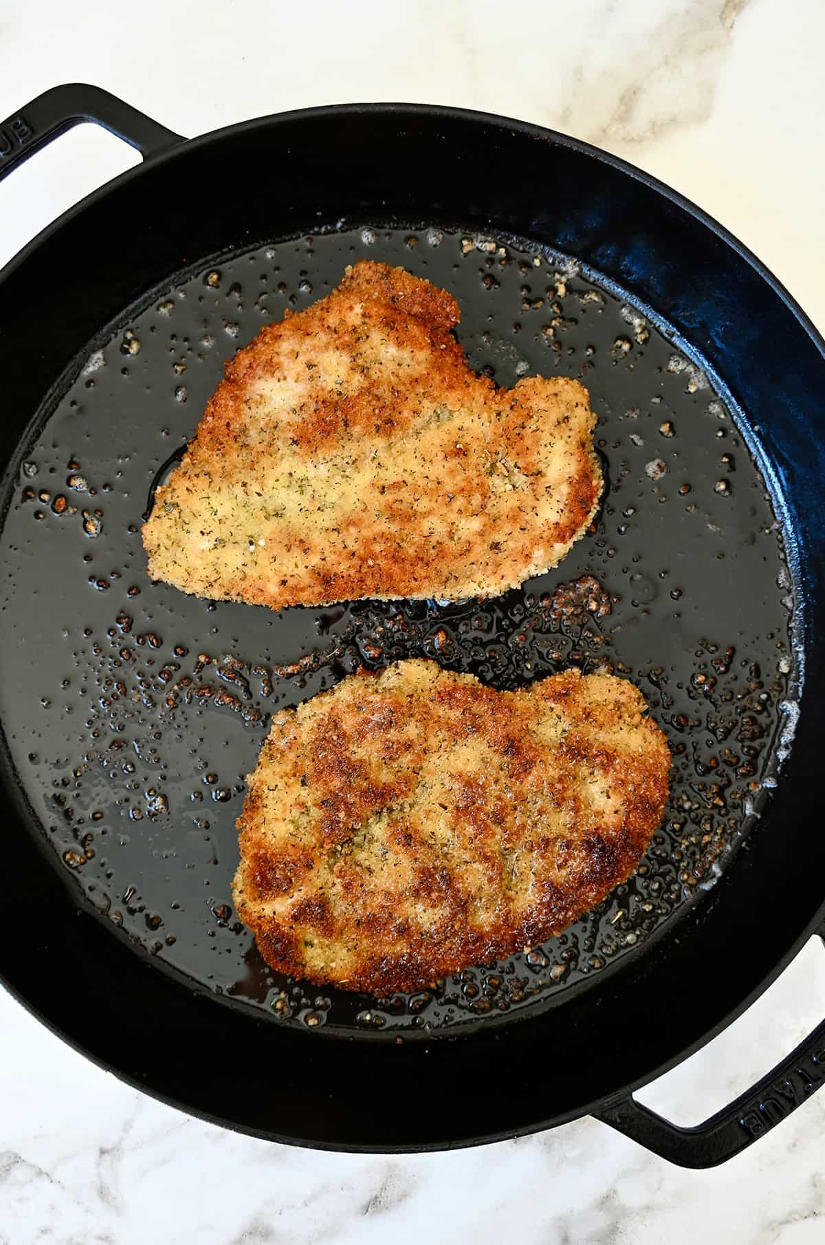 Two pan-fried chicken cutlets in a cast iron skillet.