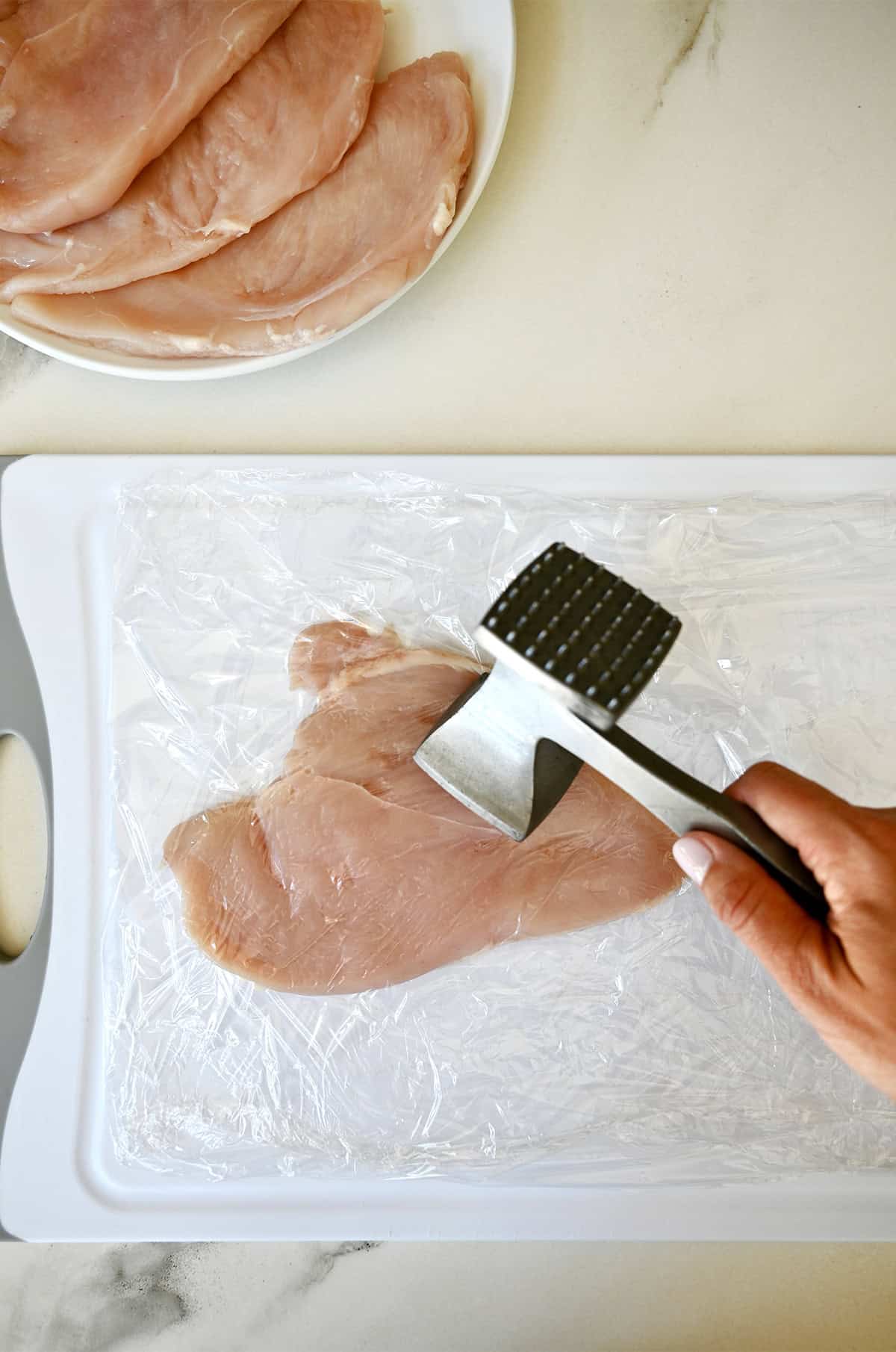 Pounding chicken breasts between two pieces of plastic wrap with a meat tenderizer.