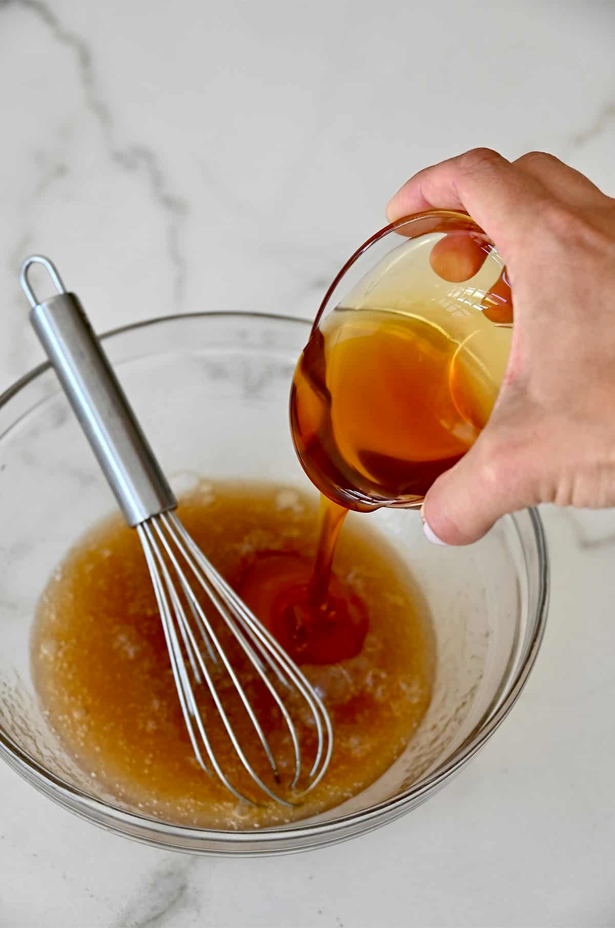 Adding honey from a small bowl to a large mixing bowl with brown sugar and egg whites.