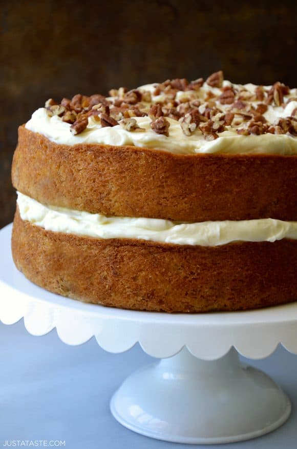 Two-Layer moist banana cake with tangy cream cheese frosting topped with pecans on cake stand