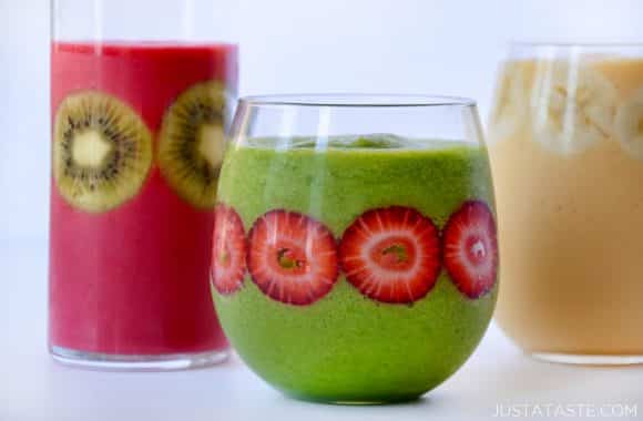 Green, pink and yellow smoothies in clear glasses with fruit