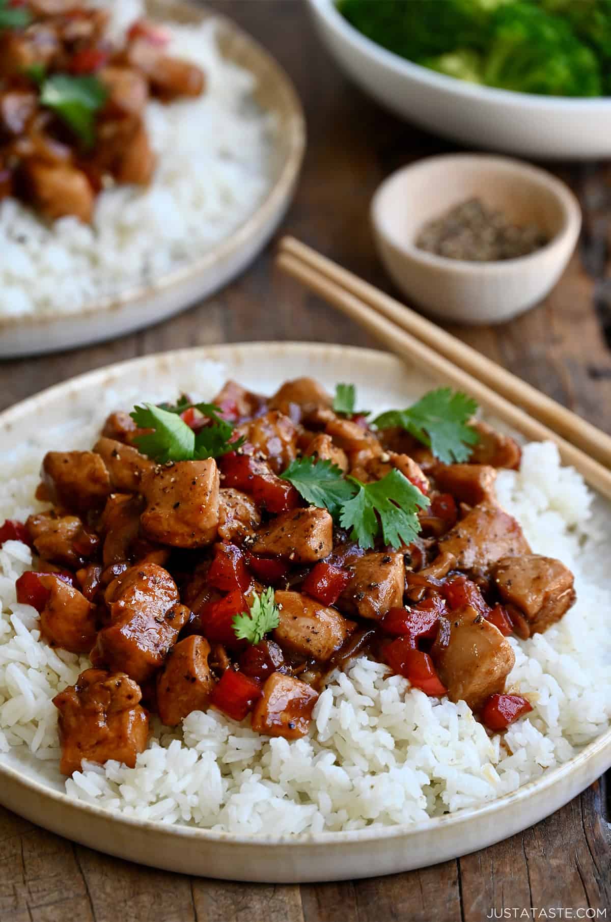 Black pepper chicken atop white rice on a plate with chopsticks.