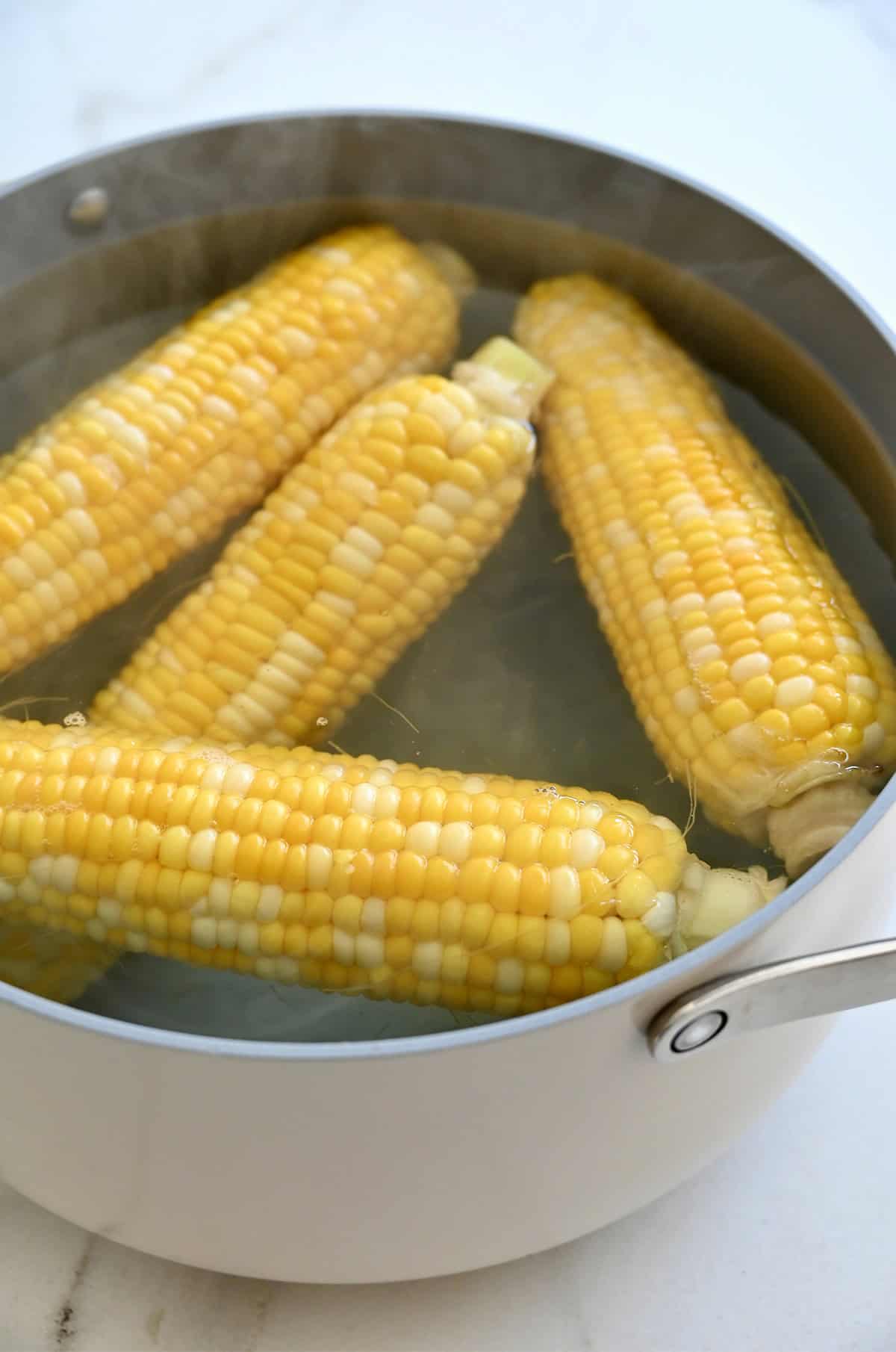 Four ears of corn are boiling in a large pot of water.