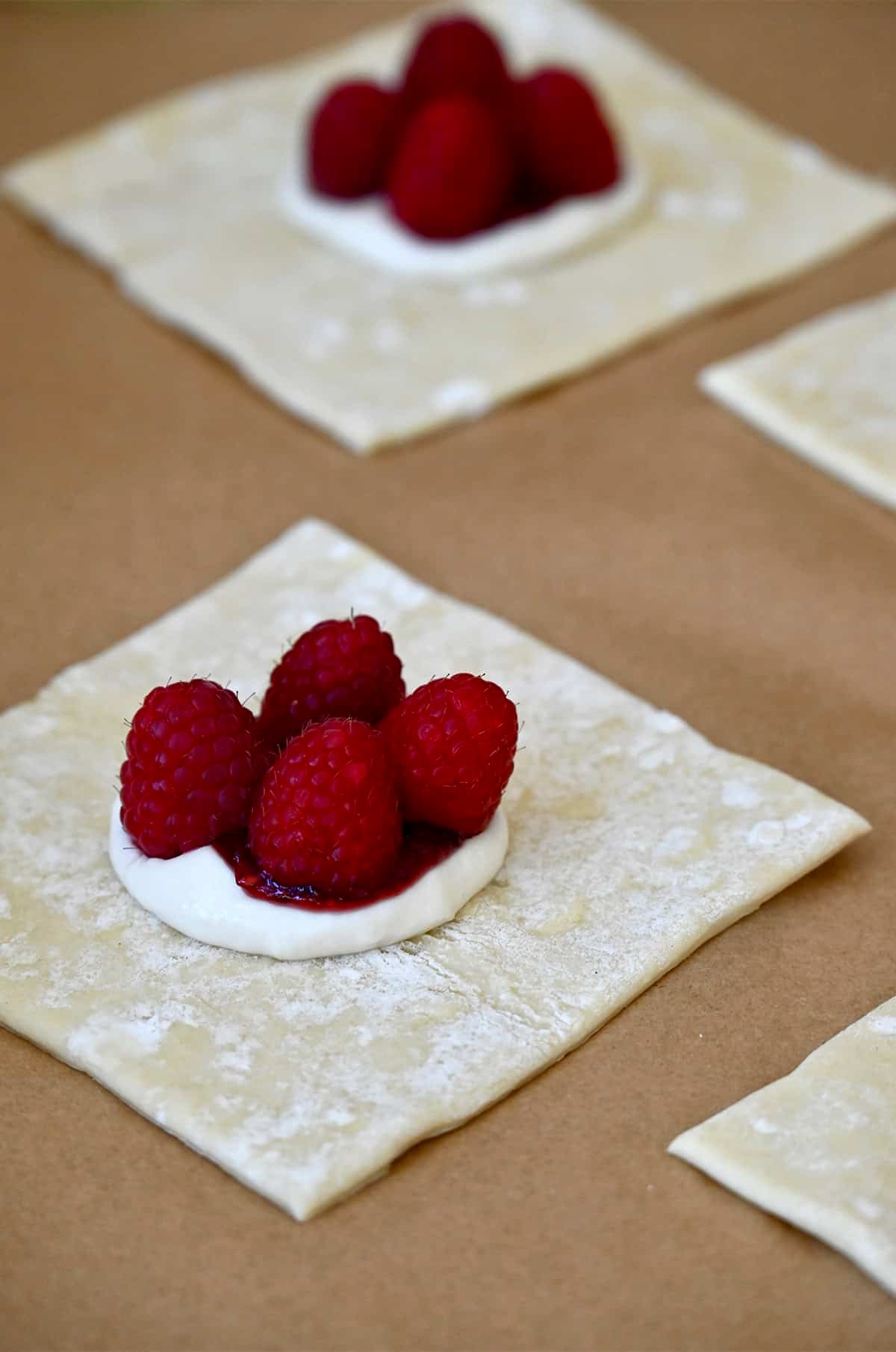 A puff pastry square topped with cream cheese, raspberry jam and four fresh raspberries.