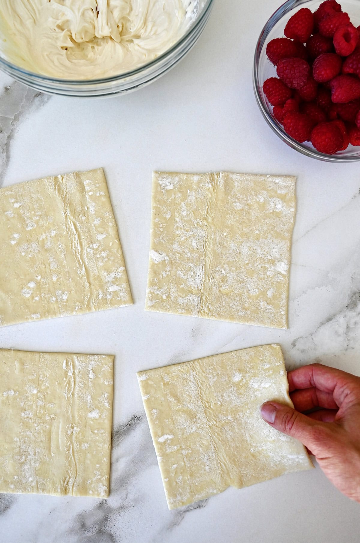 Puff pastry squares on a lightly floured marble surface.