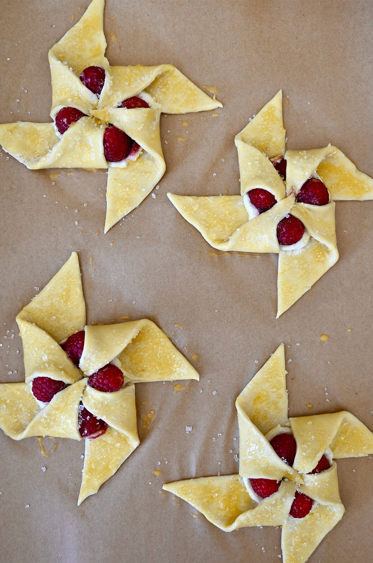Pinwheel pastries brushed with egg wash and sprinkled with sanding sugar on a baking sheet.