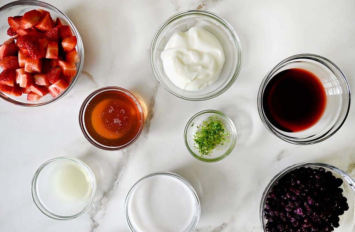 Small glass bowls containing the ingredients to make red, white and blue fruit popsicles