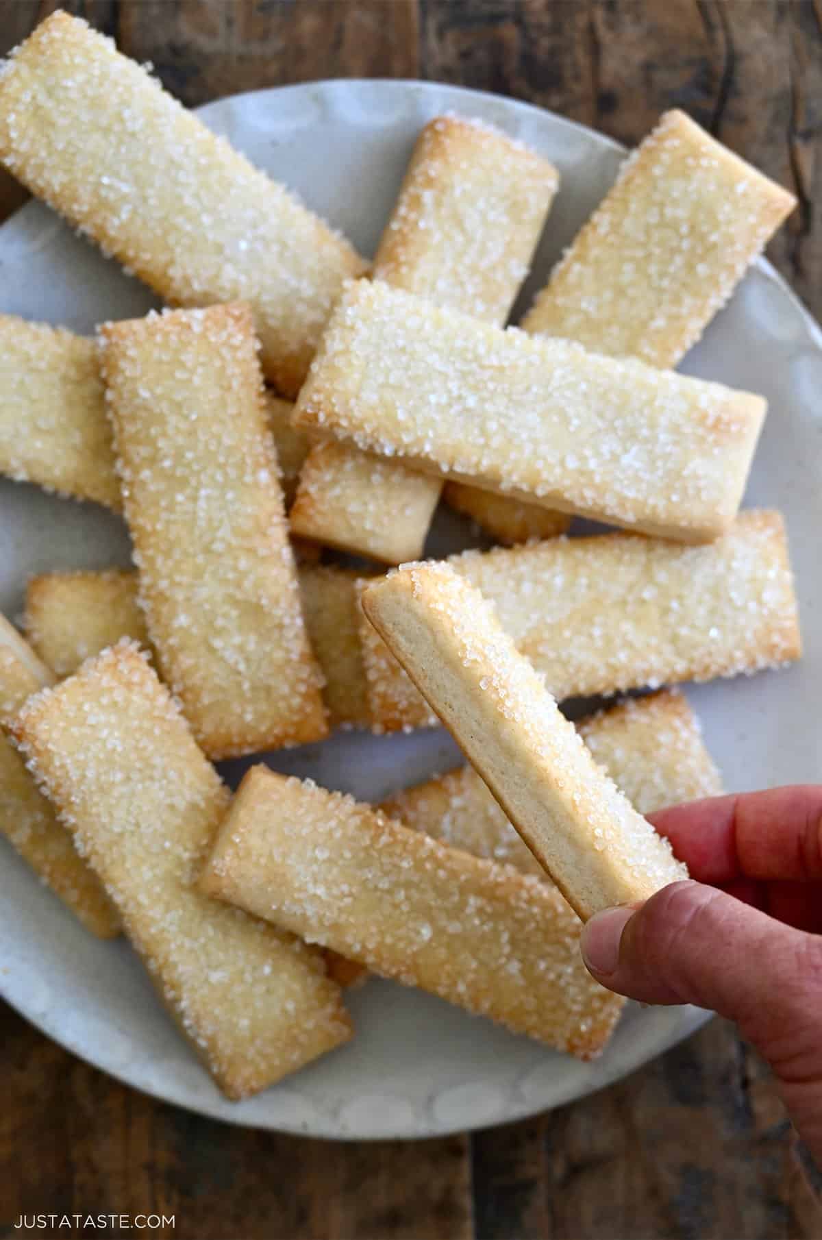 A hand holds a pie crust cookie over a plate of cookies.