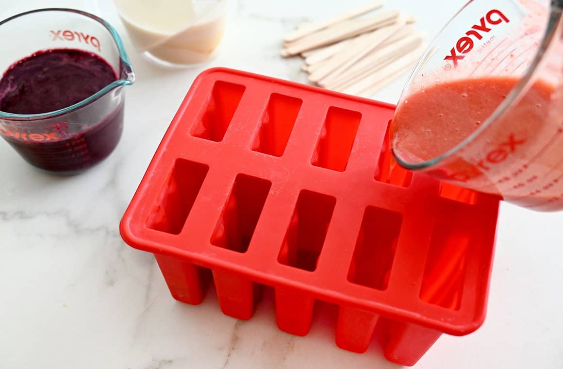 Strawberry puree being poured into a red popsicle mold