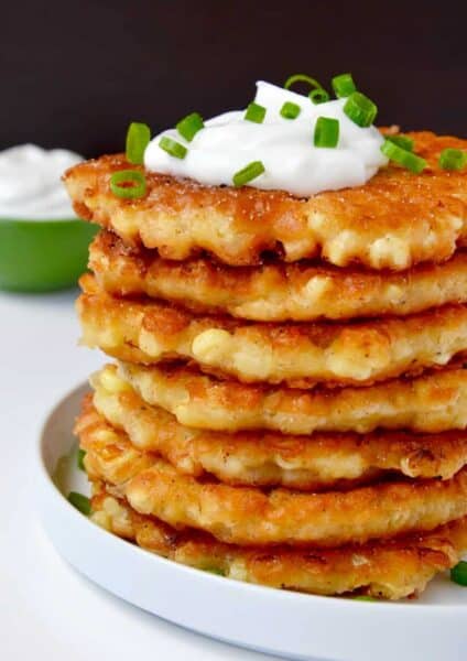 A tall stack of crispy corn fritters topped with a dollop of sour cream and chopped green onions.