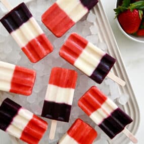 A white platter topped with crushed ice and red, white and blue popsicles