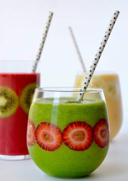 Three types of fruit smoothies in glasses with fruit stuck inside