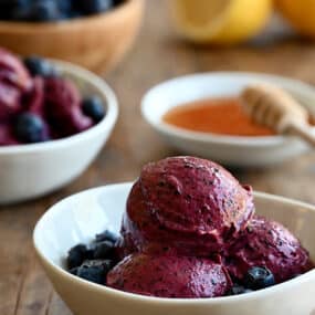 Three scoops of blueberry frozen yogurt in a white bowl with fresh blueberries