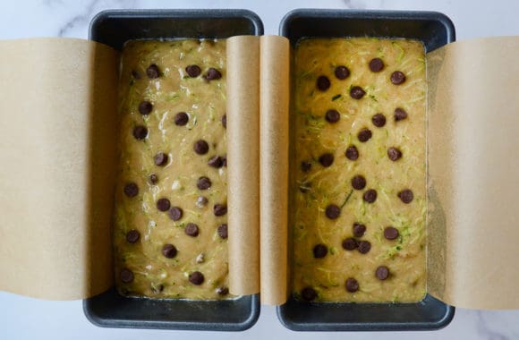 Two bread pans lined with parchment paper and filled with bread batter