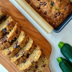 One loaf of Zucchini Chocolate Chip Bread sliced next to another loaf in a parchment paper-lined bread pan