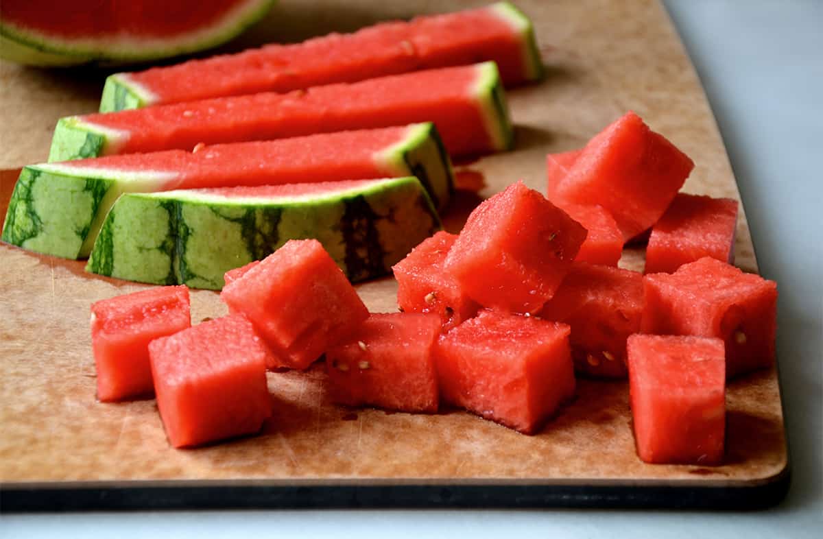 Cubed watermelon next to the rind on a wood cutting board.