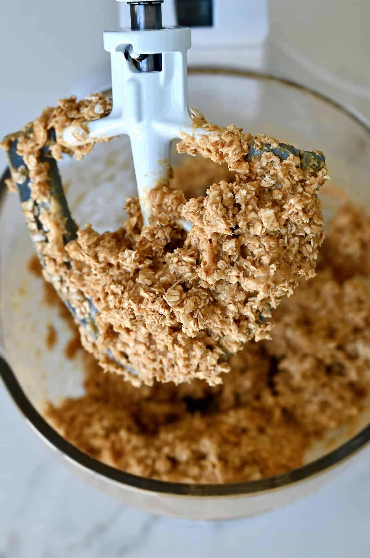 An oatmeal peanut butter mixture covering the paddle attachment of a stand mixture.