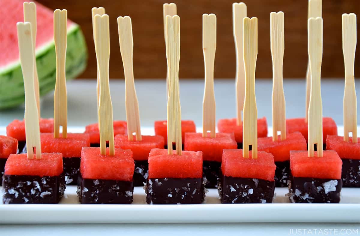 Perfect rows of watermelon bites dipped in chocolate and sprinkled with sea salt on a white serving platter.