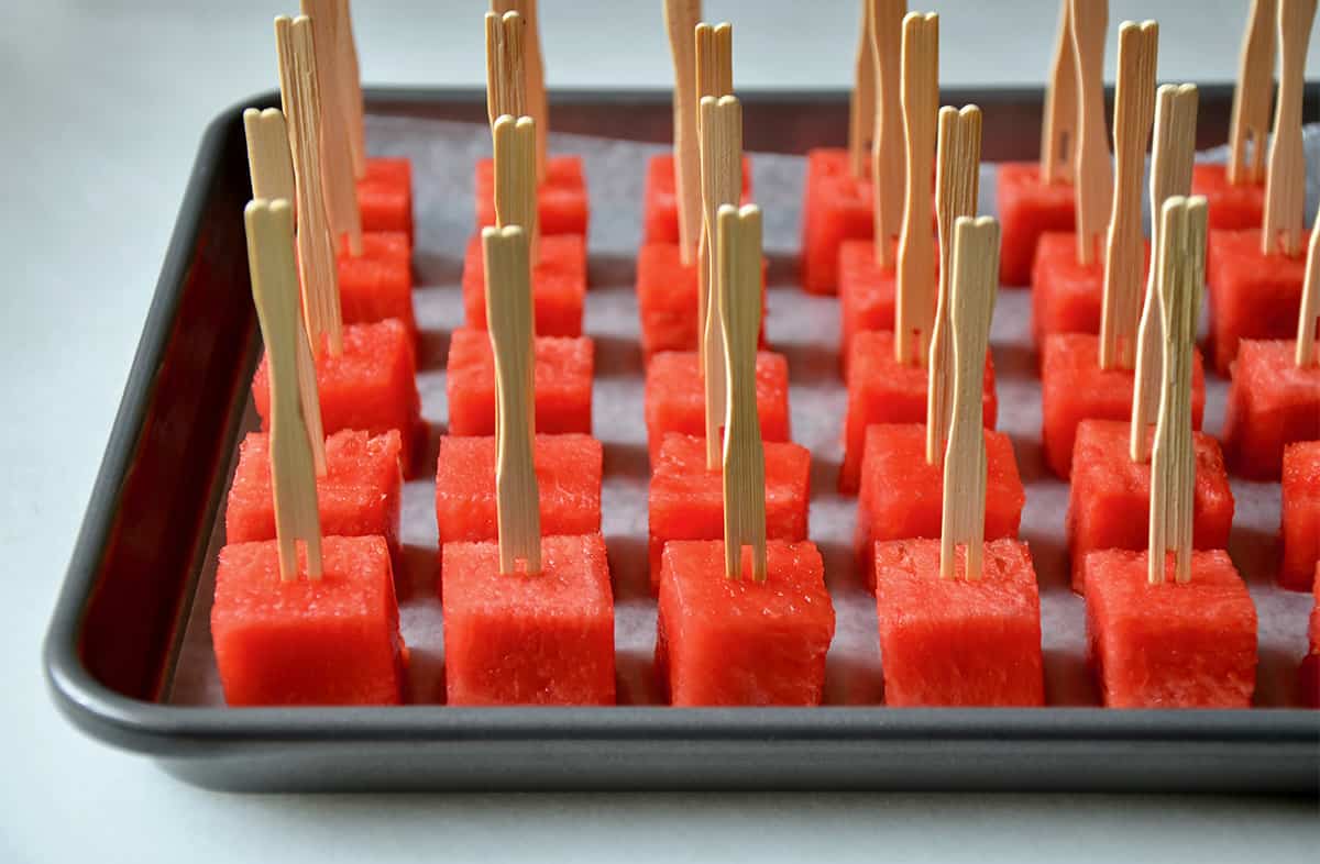 Watermelon cubes with toothpicks on a wax paper-lined baking sheet.