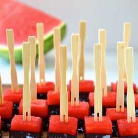 Frozen chocolate-covered watermelon bites with sea salt and toothpicks on a serving plate.