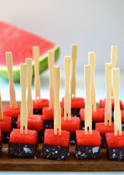 Frozen chocolate-covered watermelon bites with sea salt and toothpicks on a serving plate.