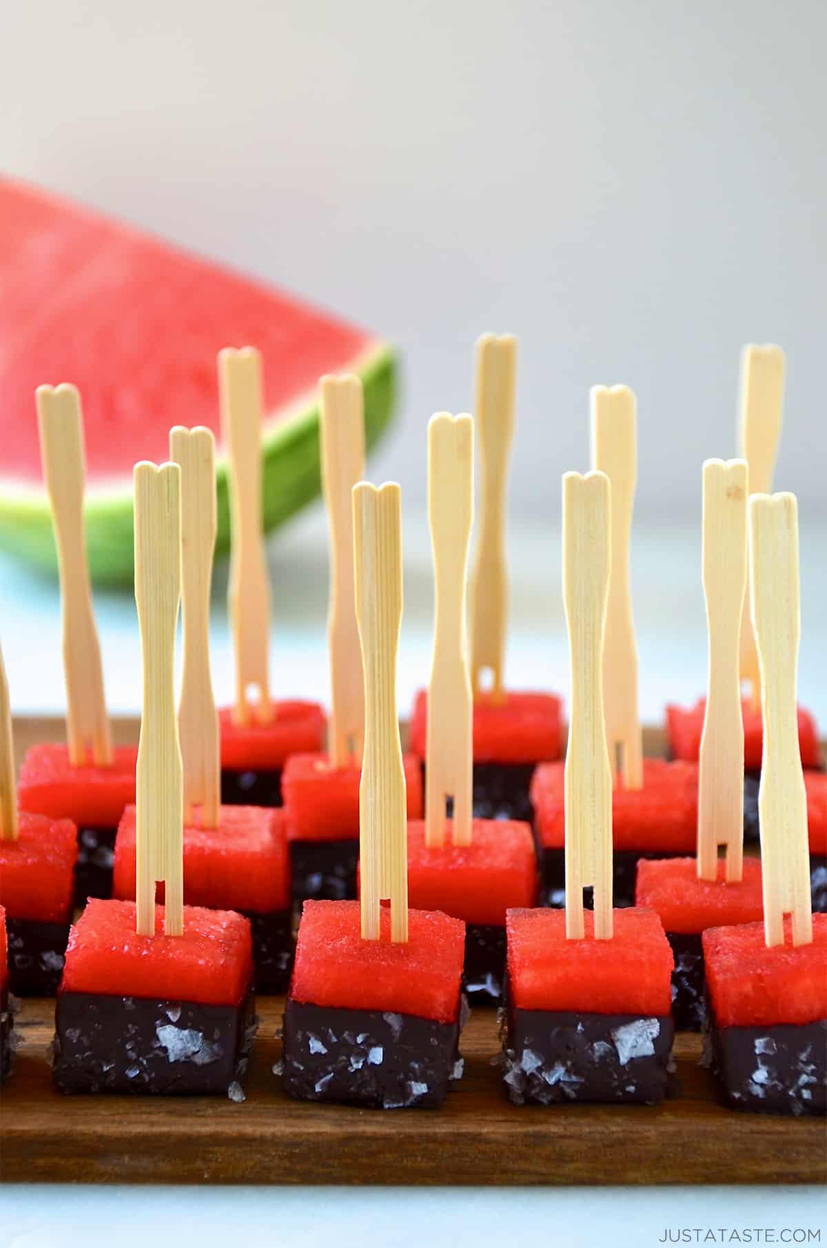 Frozen chocolate-covered watermelon bites with sea salt and toothpicks on a serving plate.