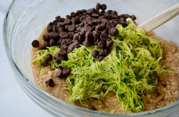 Clear bowl containing zucchini bread batter, grated zucchini and chocolate chips