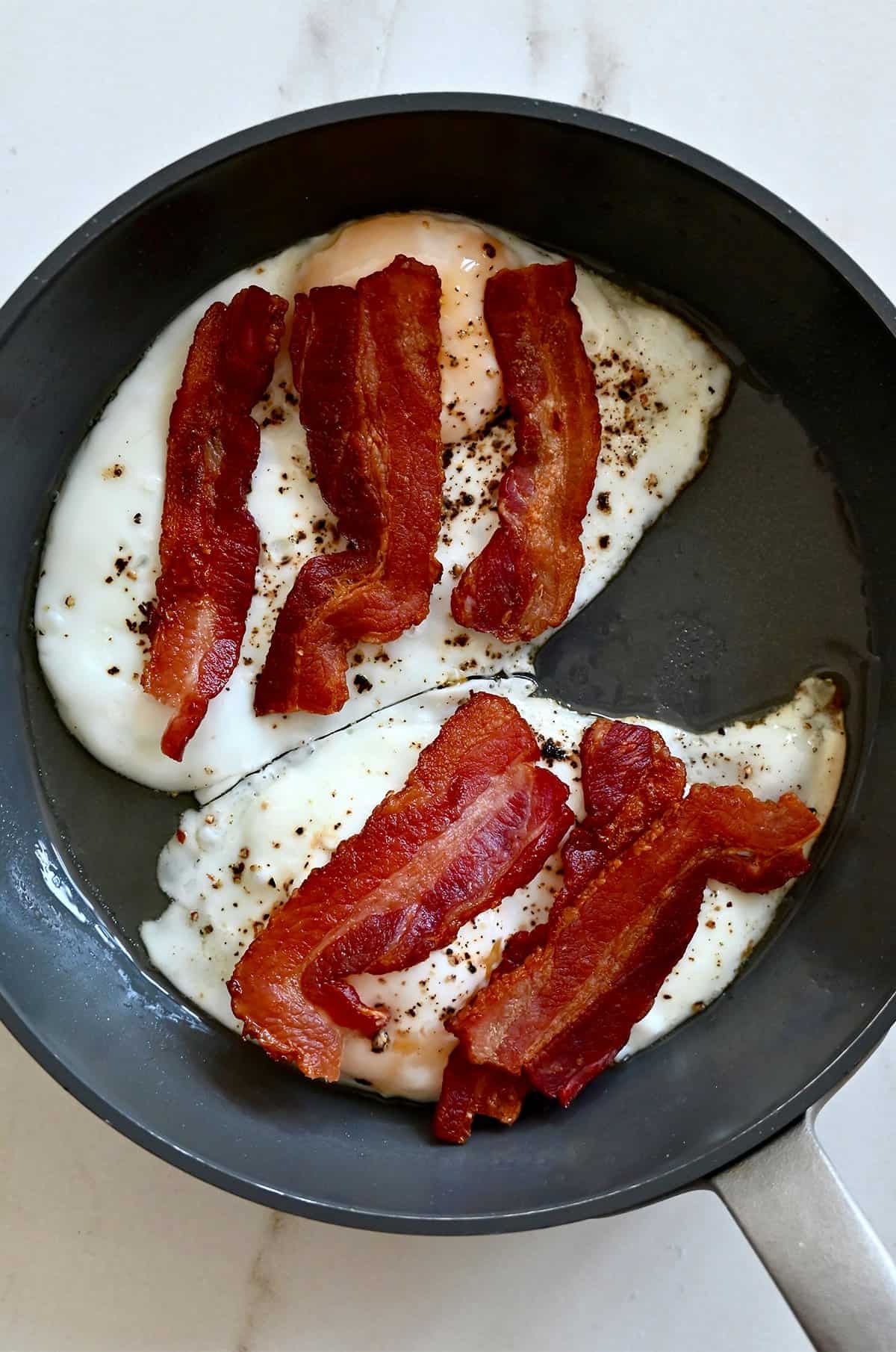 Two fried eggs topped with strips of crispy bacon in a skillet.