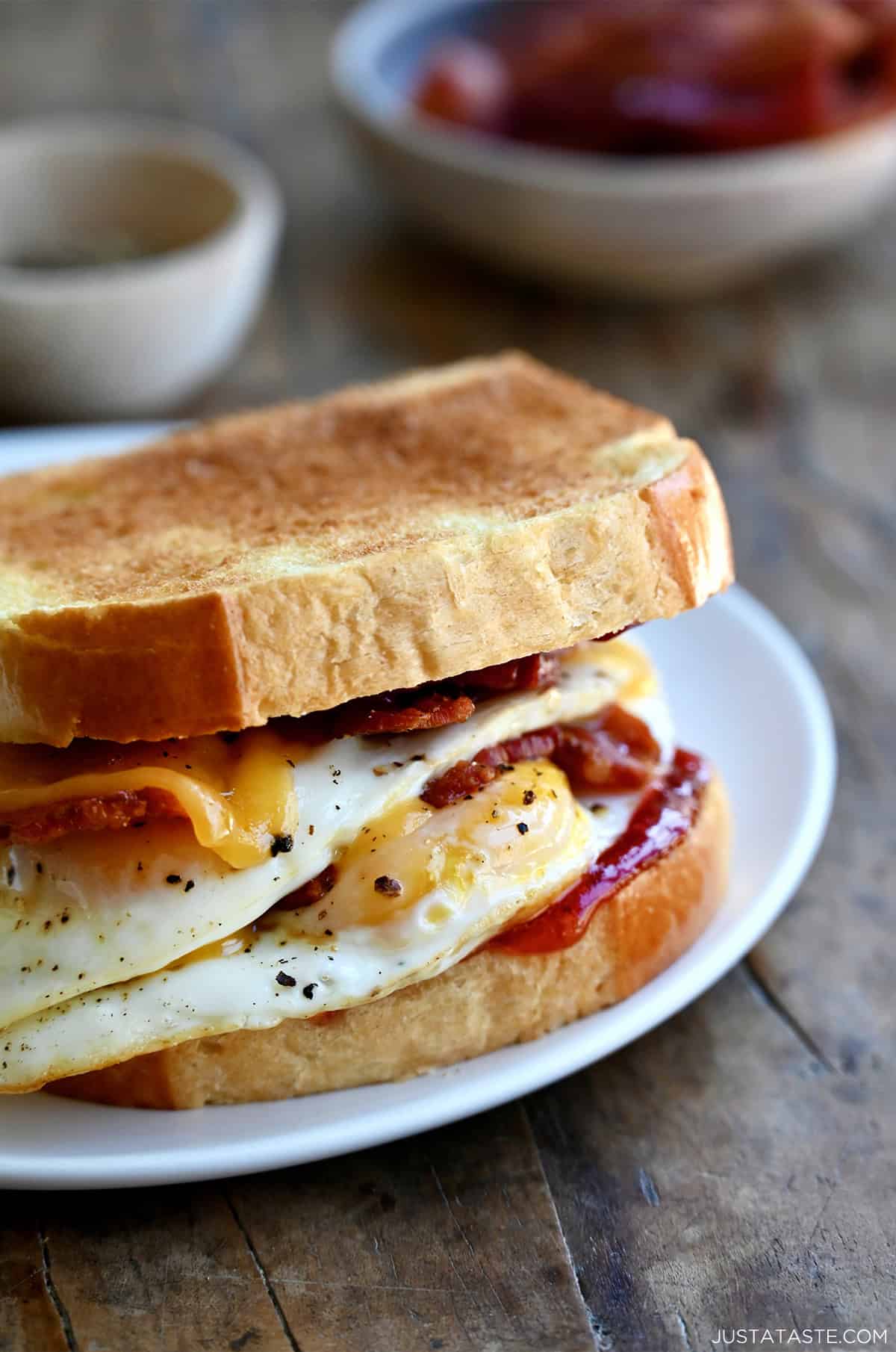 Breakfast sandwich with two fried eggs, crispy bacon, cheddar cheese and strawberry jelly on brioche toast.