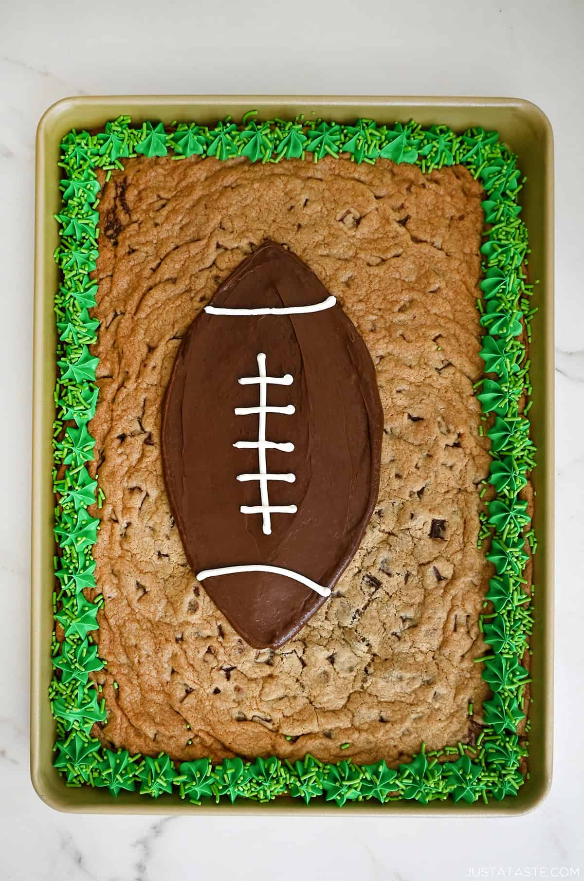 Chocolate chip cookie cake decorated with green buttercream and a chocolate frosting football for game day.
