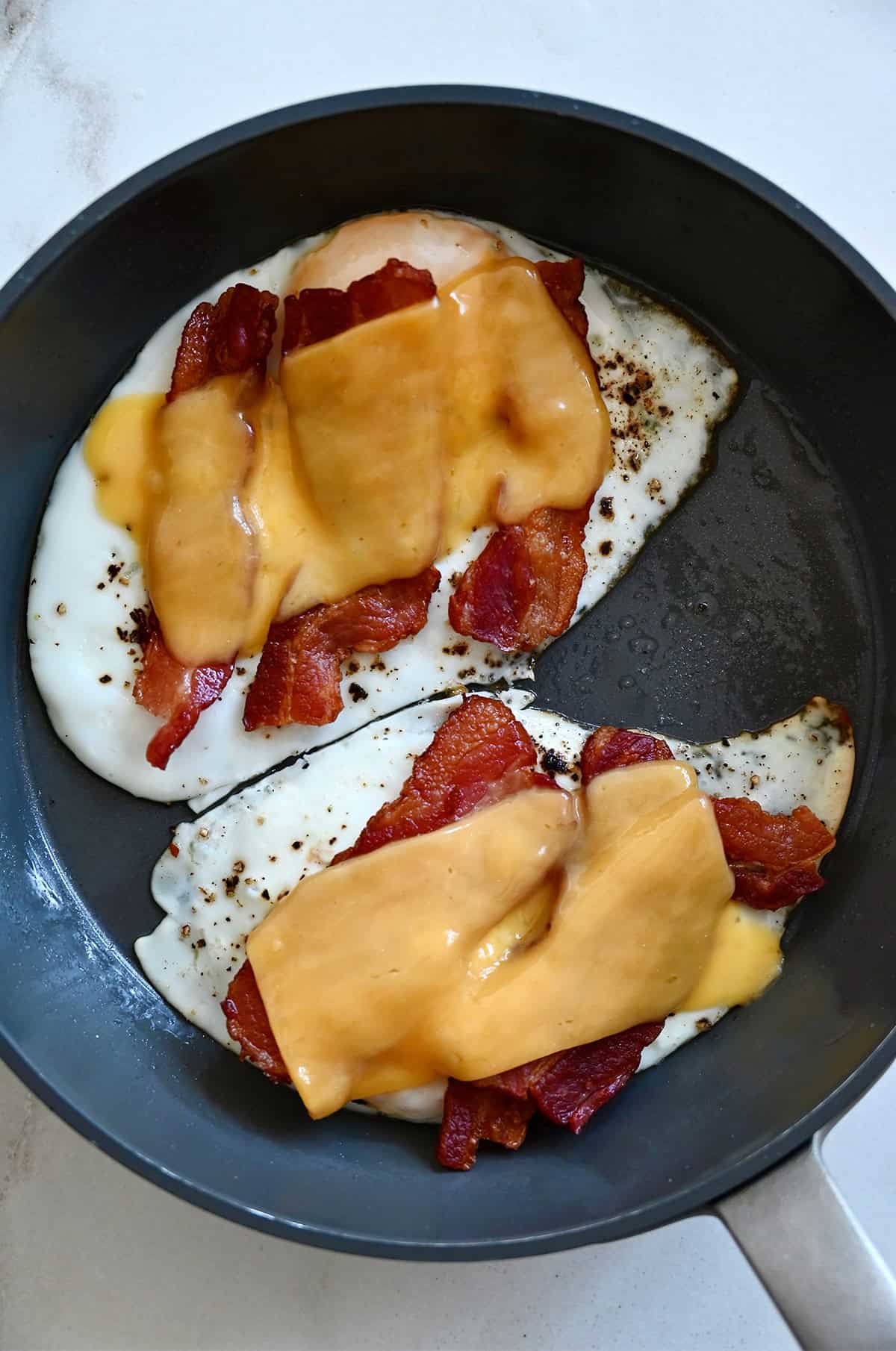 Melted cheese atop cooked bacon and two fried eggs in a skillet.