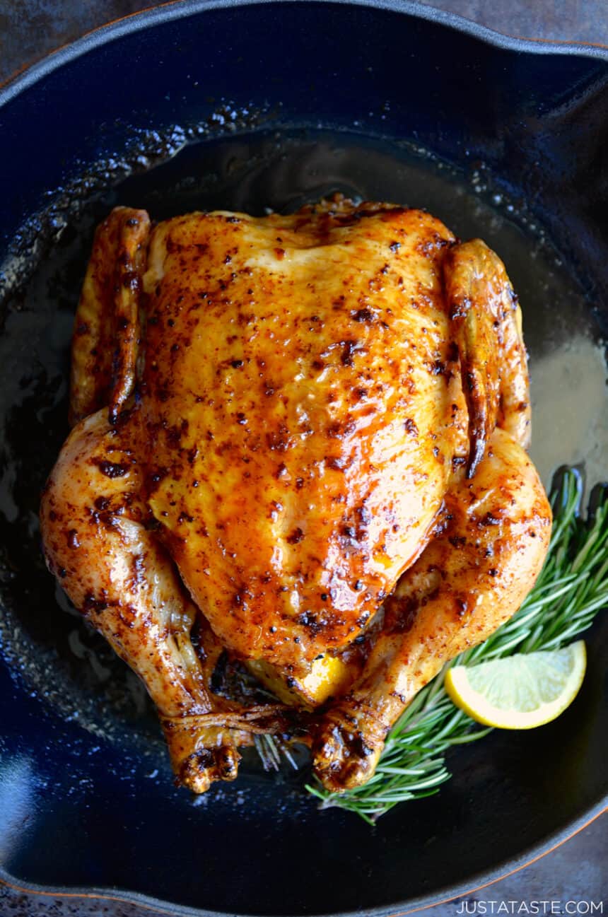 A top-down view of a whole roast chicken with fresh rosemary sprigs and a lemon wedge in a cast-iron skillet