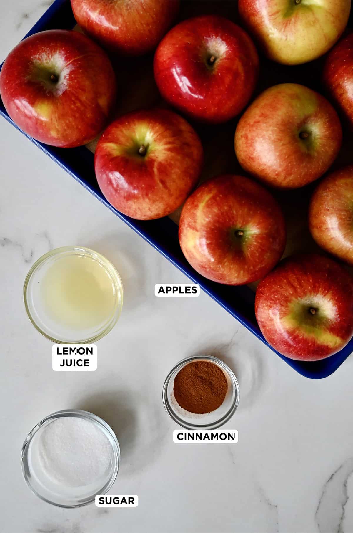 Honeycrisp apples next to small bowls containing cinnamon, lemon juice and sugar.