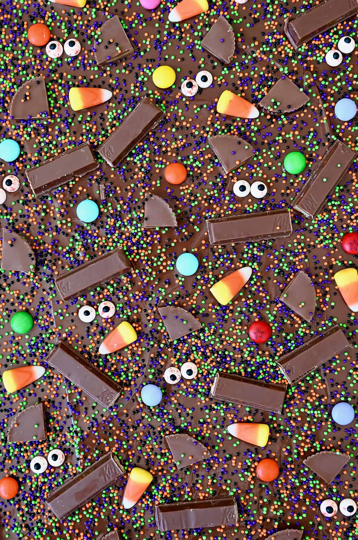Halloween candy bark with festive sprinkles, M&Ms, candy corn, Reese's and KitKat bars before being broken into pieces.