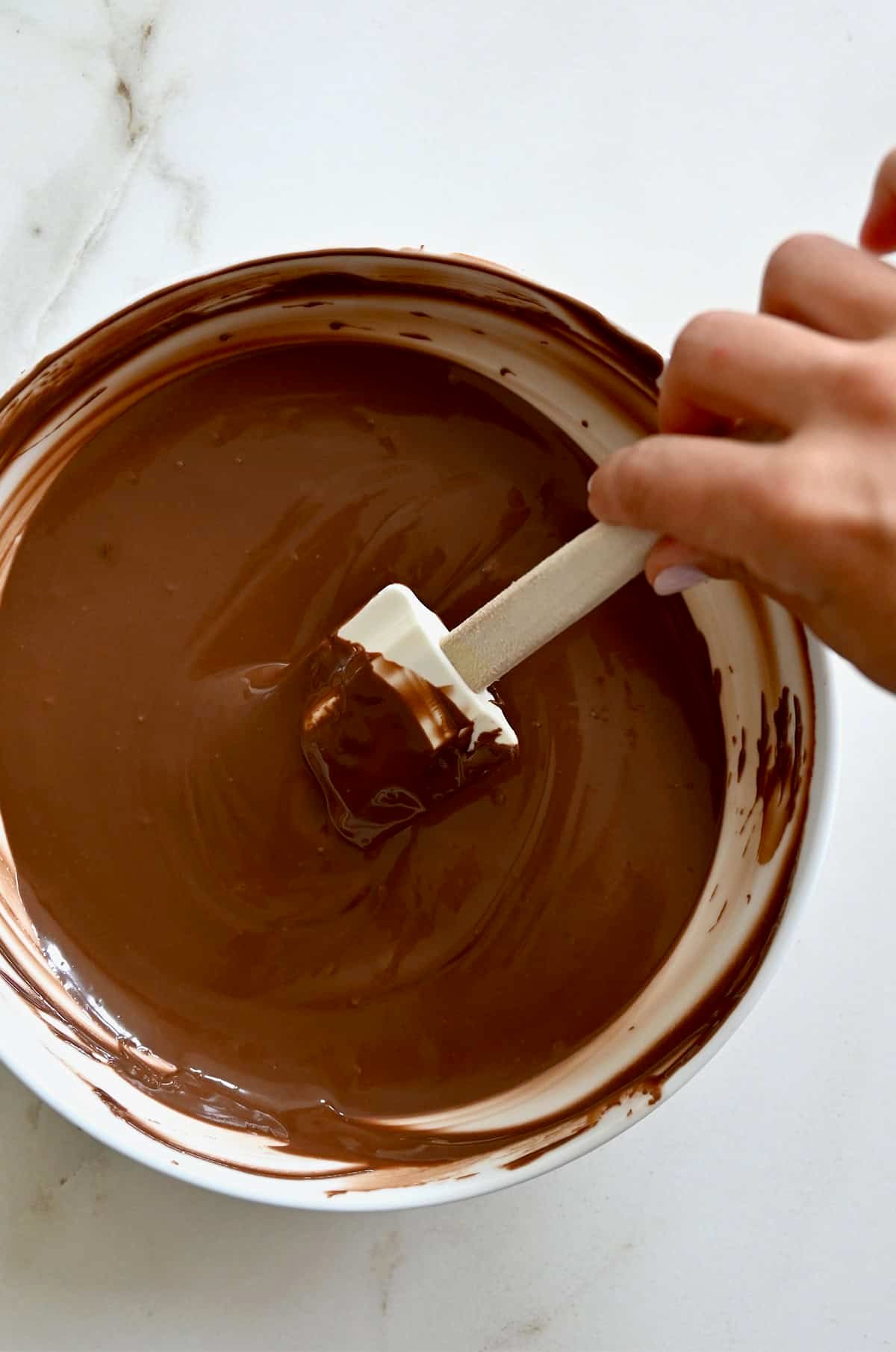 Melted chocolate in a glass bowl being stirred with a spatula.