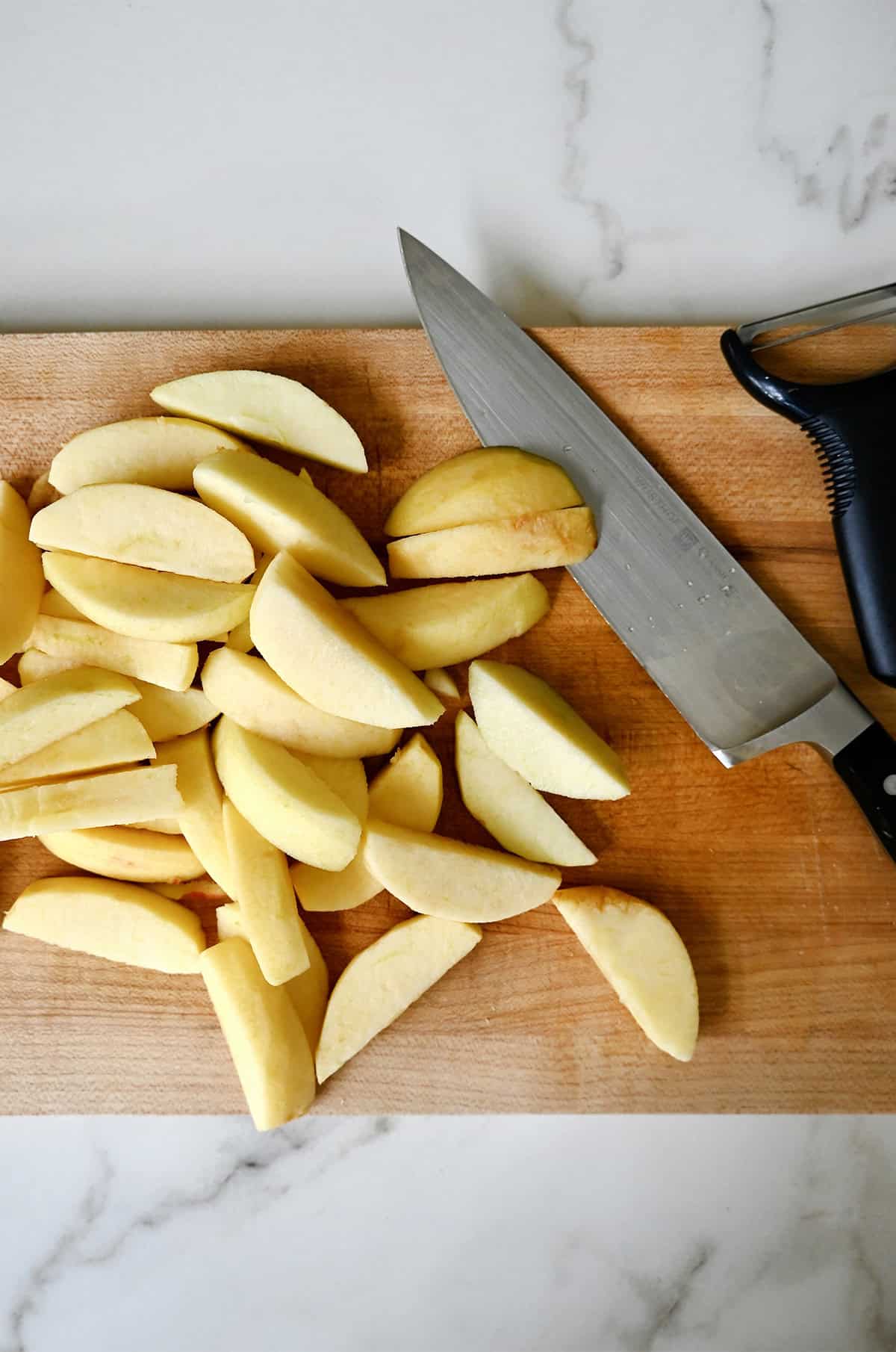 Peeled and cut apples on a cutting board with a sharp knife and vegetable peeler.